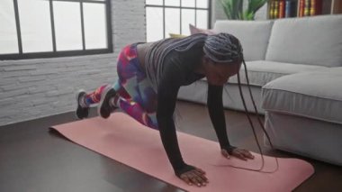 Saçları örgülü, yoga minderinin üstünde egzersiz yapan Afro-Amerikalı bir kadın.