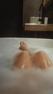 Rahat bir kadın, sakin bir banyo ortamında köpük banyosundan zevk alır, sükunet ve kendine bakımı çağrıştırır..