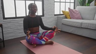 Afrikalı bir Amerikalı kadın evde yoga yapıyor, modern bir oturma odasında kondisyon ve sükunet sergiliyor..