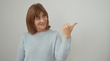 Neşeli orta yaşlı, kısa saçlı, kendine güvenen, başparmak kaldıran, rahat bir süveter giyip kenarı işaret eden bir kadın. Işıl ışıl beyaz bir arkaplanda.