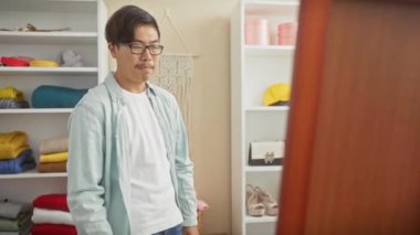 Genç Asyalı bir adam, hareketlerini yansıtan bir aynayla gündelik bir odada giyiniyor..