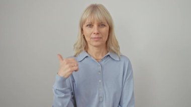 Neşeli, kendine güvenen, tişört giyen, ayakta duran ve baş parmağıyla işaret eden sarışın kadın. Geniş bir gülümseme, izole edilmiş beyaz bir arka plana karşı ağzını açık gösteriyor..