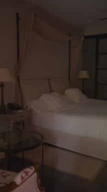 Zarif bir yatak odası, komodinleri, masa lambası ve rahat bir iç atmosferi olan cam bir masa..