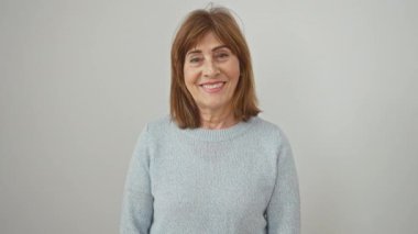 Neşeli orta yaşlı bir kadın mükemmel bir gülümsemeyle kendine güveni yayıyor, şık bir süveter giyiyor, izole edilmiş soğuk bir arka plana karşı..