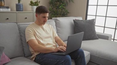 Genç İspanyol adam bilgisayarını kapatıp kameraya gülümsüyor ve modern bir oturma odasında kanepede oturuyor..