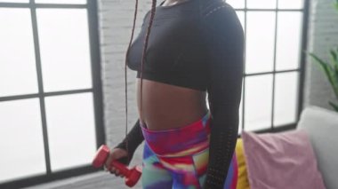 Afrika kökenli Amerikalı bir kadın evde dambıllarıyla egzersiz yapıyor, spor yapıyor ve ev ortamında sağlıklı bir yaşam sürüyor..