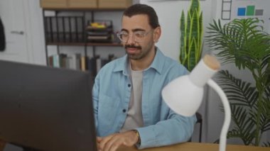 Masasında bir lamba ve bitkilerle ofis ortamında çalışan genç bir adam.