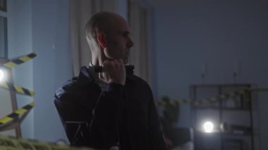 Sakallı kel dedektif, elinde fenerle karanlık bir suç mahallini inceliyor..