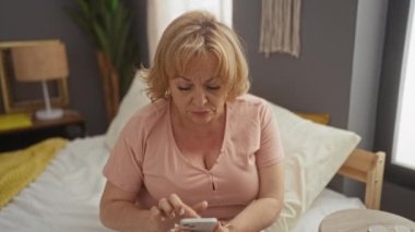 Yaşlı, beyaz bir kadın, yatak odasında, yatağında telefonla konuşuyor..