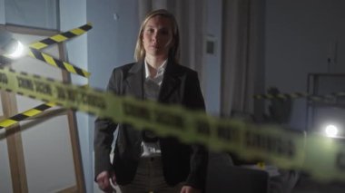 Ciddi kadın dedektif, karanlık kapalı bir ortamda, uyarı bandı ve loş ışıkla suç mahallini araştırıyor.