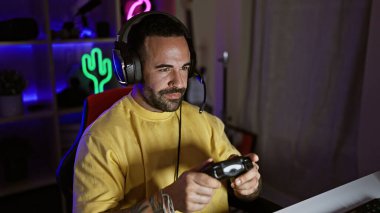 Odaklanmış, sakallı, gece karanlık bir odada video oyunu oynayan kulaklık takan İspanyol bir adam..