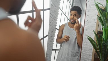Afrikalı Amerikalı adam modern dairenin oturma odasındaki aynada tenini kontrol ediyor. Endişelerini dile getiriyor..