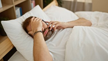 Yatakta, kapalı alanda uzanmış, düşünceli bir ifadeyle telefonuna bakan, beyaz saçlı, olgun bir İspanyol..