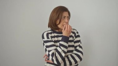 Çizgili kazak giyen gergin İspanyol kadın tırnak yiyor, anksiyete sorunu yüzünden stresli, beyaz arka planda izole edilmiş.