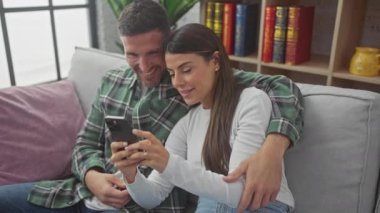 Sevgi dolu bir İspanyol çift evdeki kanepelerinde dinleniyor, akıllı telefondan gülümsüyor..