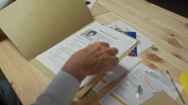 Üst düzey bir adam, dedektifin ofisindeki ahşap bir masada kanıt ve belgeleri inceler ve ipucu arar..