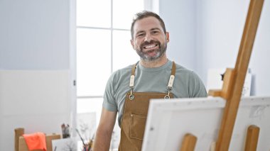 Stüdyoda gri saçlı, önlük giymiş, iç mimari ortama gülümseyen orta yaşlı yakışıklı bir adam..