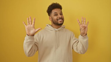 Afrikalı Amerikalı adam sarı arka planda izole edilmiş 9 numaralı jesti yapıyor. Parmaklarını gösteriyor.