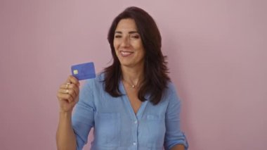 Elinde kredi kartıyla gülümseyen bir kadın soyutlanmış pembe arka planda mutlu bir orta yaşlı.