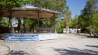 Açık hava bulanık çardak sahnesi. Yumuşak odak arkaplanı açık bir gökyüzünün altında. Çerçevelenmiş yemyeşil ağaçlar ve asfalt bir patika.