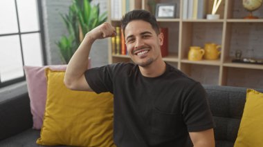 Gülümseyen genç bir İspanyol adam oturma odasında kol kaslarını esnetiyor..
