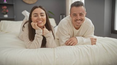 Sıcak kıyafetler giymiş neşeli bir çift, iyi döşenmiş bir yatak odasında uzanır, sevgi ve mutluluk saçar..