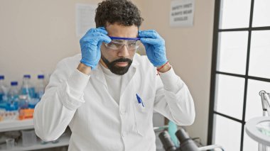 Bir adam güvenlik gözlüklerini, araştırma ve sağlık hizmetlerini sembolize eden parlak ışıklı bir laboratuvarda ayarlar..