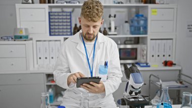Modern bir laboratuvarda sakallı beyaz erkek bilim adamı tablet kullanıyor..