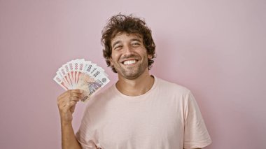 Handsome hispanic man smiling with icelandic kronur in front of a pink wall. clipart