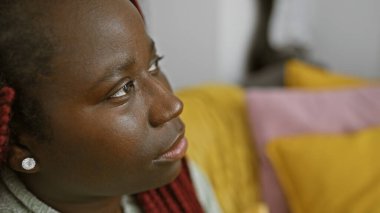 Örgü örmüş, evinde güzelliğini ve tarzını sergileyen düşünceli Afrikalı Amerikalı bir kadının portresi..