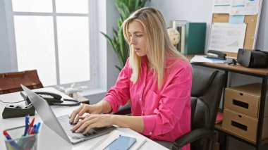 Modern ofis ortamında dizüstü bilgisayarda daktilo eden konsantre genç beyaz kadın..