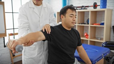 Erkek bir fizyoterapist hastaya iyi donanımlı, modern bir klinikte rehabilitasyon egzersizlerinde rehberlik eder..