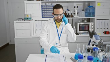 Beyaz laboratuvar önlüklü, sakallı İspanyol bir adam araştırma laboratuarında telefonla bulguları tartışıyor..