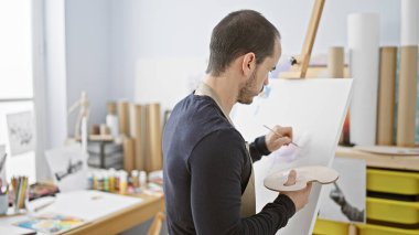 Parlak bir sanat stüdyosundaki tuvale yoğunlaşmış bir adam yaratıcılığı ve sanatsal ifadeyi somutlaştırıyor..