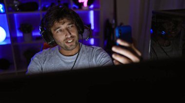 Evdeki karanlık oyun odasında akıllı telefon kullanan kulaklıklı yakışıklı bir adam..