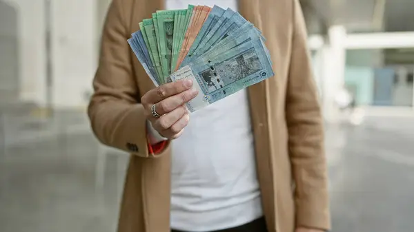 stock image A young man displays various malaysian ringgit notes on a city street, exhibiting urban financial transactions.