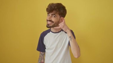 Gülümseyen, genç İspanyol adam parmaklarıyla bir telefon hareketi yapıyor, iletişim konsepti için izole edilmiş sarı arka planda duruyor.