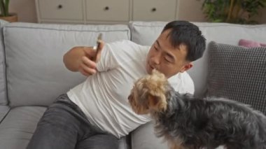 Genç Asyalı bir adam köpeğiyle birlikte Çin 'de rahat bir oturma odasında selfie çekiyor..