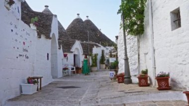 Yeşil elbiseli genç bir İspanyol kadın güneşli bir günde eski Alberobello, Puglia, İtalya 'daki Trulli evlerle dolu pitoresk bir caddede yürüyor..