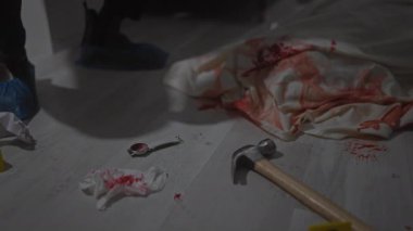 Dedektif, kapalı bir suç mahallinde kan, çekiç ve kelepçe inceler.