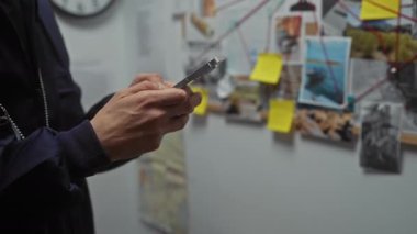 Bir dedektifin ofisinde elinde büyüteçle kanıtları inceleyen, notlar ve fotoğraflarla dolu genç bir adamın yakın çekimi..