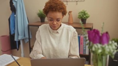 Mutsuz Afro-Amerikan kadın evde, masada oturuyor ve olumsuz bir hareket sergiliyor. Kızgın, kötü bir ifadeyle aşağıya bakıyor..