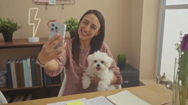 Gülümseyen bir kadın beyaz Bizon köpeğiyle evde selfie çekiyor..