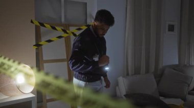 Odaklanmış bir adam dikkat bandı ve el feneriyle loş ışıklandırılmış bir suç mahallini araştırır..