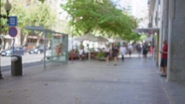 Arka planda bulanık bir sahne, şortlu bir kadın ve kalabalık bir caddede ağaçlar ve binalarla yürüyen insanlar.