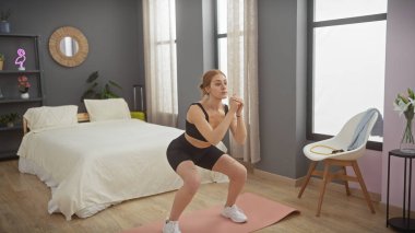 Modern bir yatak odası ortamında egzersiz yapan genç bir kadın refah ve iç tasarım estetiğine odaklanıyor..
