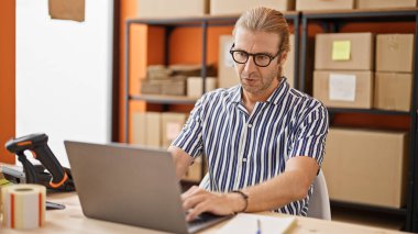 Depoda dizüstü bilgisayarla çalışan gözlüklü yakışıklı bir adam..