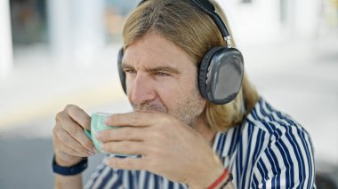 Kulaklıklı sarışın bir adam dışarıda kahve yudumluyor, günlük hayat ve tarz sergiliyor..