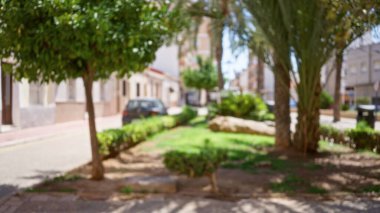 Açık gökyüzü altındaki yerleşim binalarıyla çevrili, ağaçlar ve bitkilerle çevrili küçük bir parkın, huzurlu bir şehir ortamını görüntülediği yer..