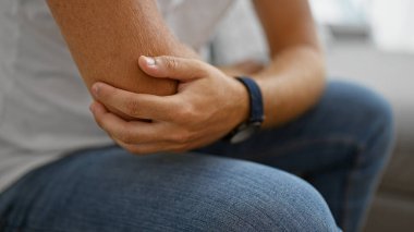 İçeride oturan genç bir adam dirseğini acı içinde tutuyor. Olası bir yaralanma ya da rahatsızlık hissi veriyor..